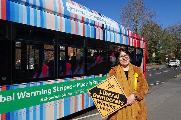 Councillor Anne Thompson holding a Lib Dem diamond by a bus